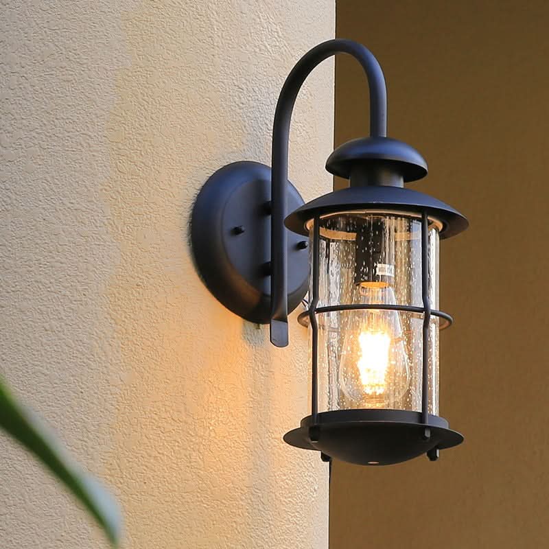 Black cylindrical outdoor sconce with seeded glass and illuminated bulb on a textured wall.